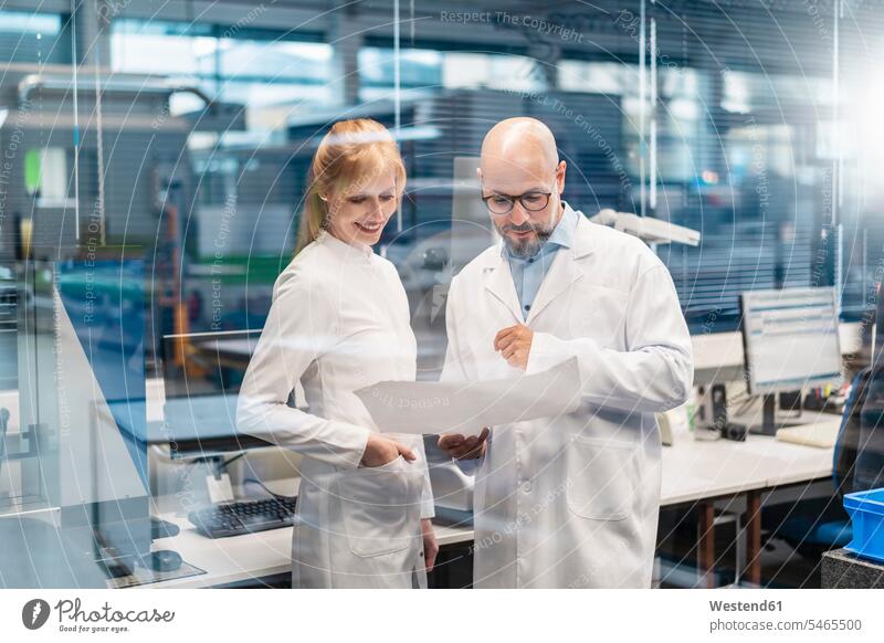 Two technicians wearing lab coats looking at plan Laboratory Coat Labcoats Lab Coat Laboratory Coats Lab Coats eyeing plans view seeing viewing technology
