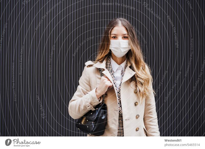 Mid adult woman with purse wearing protective face mask against black wall color image colour image outdoors location shots outdoor shot outdoor shots day
