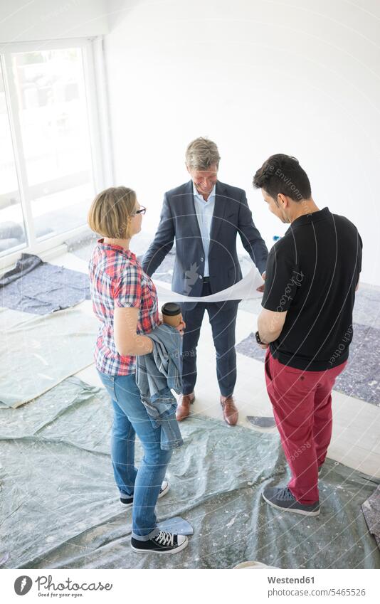 Man in suit and couple looking at blueprint in unfinished building Fullsuit suits full suit construction site Building Site sites Building Sites