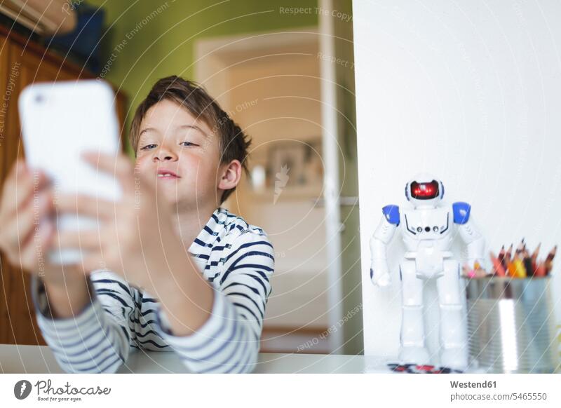 Boy doing homeschooling and using smartphone at home Tables desks toys robots telecommunication phones telephone telephones cell phone cell phones Cellphone