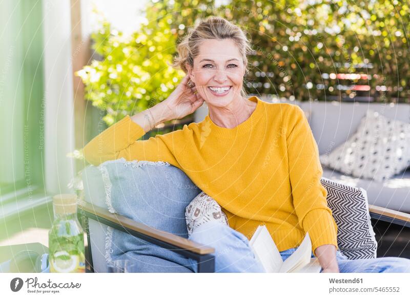 Portrait of happy mature woman sitting on terrace with book Bottles Glass Bottles Crockery Tableware Drinking Glass Drinking Glasses books jumper sweater