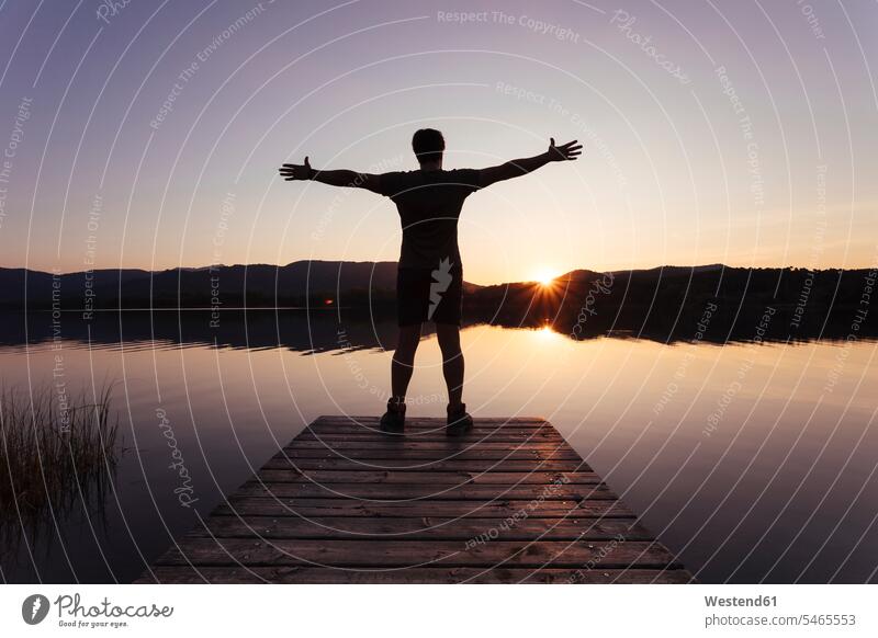 Silhouette of a man with open arms on a wooden footbridge at dusk human human being human beings humans person persons caucasian appearance caucasian ethnicity