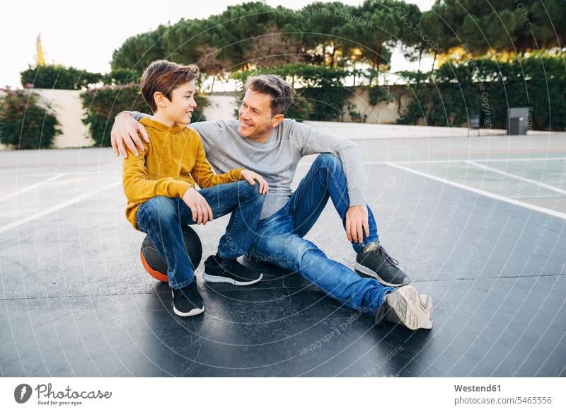 Father embracing son on basketball outdoor court sports field sports fields basketballs sitting Seated sons manchild manchildren embrace Embracement hug hugging