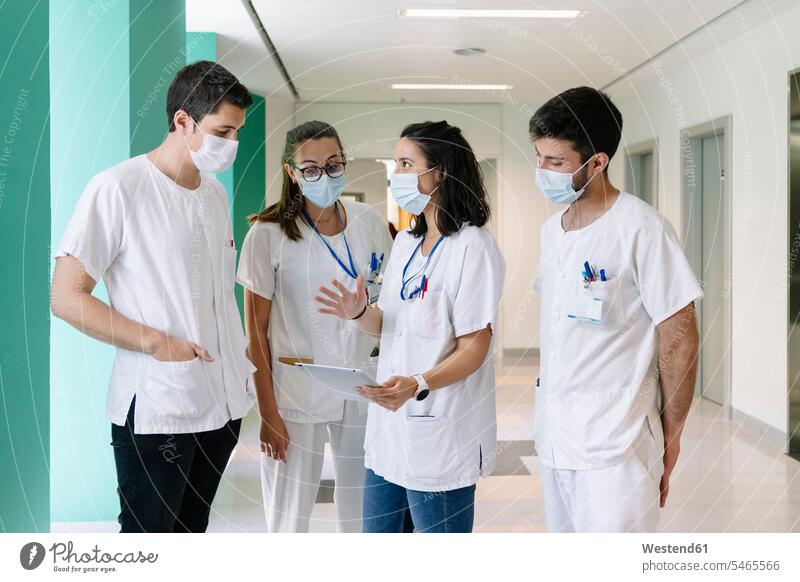 Doctors wearing surgical masks discussing over digital tablet while standing in hospital color image colour image Spain indoors indoor shot indoor shots