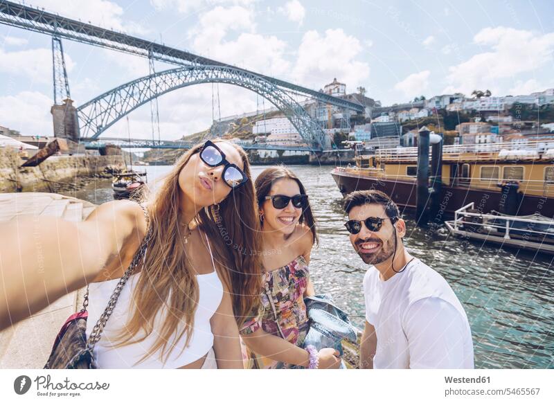 Cheerful young friends taking selfie against Douro River in city, Porto, Portugal outdoors location shots outdoor shot outdoor shots color image colour image
