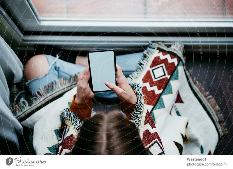 Girl with blanket using mobile phone while sitting by window at home color image colour image indoors indoor shot indoor shots interior interior view Interiors