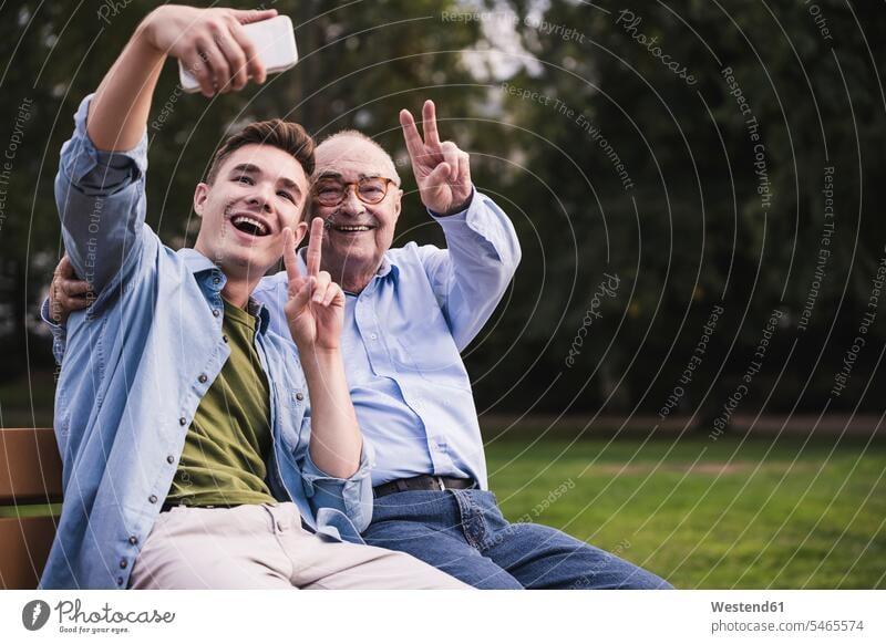 Senior man and grandson sitting together on a park bench taking selfie with smartphone human human being human beings humans person persons caucasian appearance