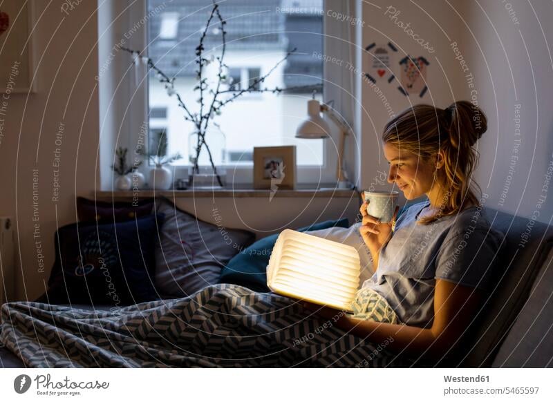 Young woman reading illuminated book on couch at home human human being human beings humans person persons caucasian appearance caucasian ethnicity european 1