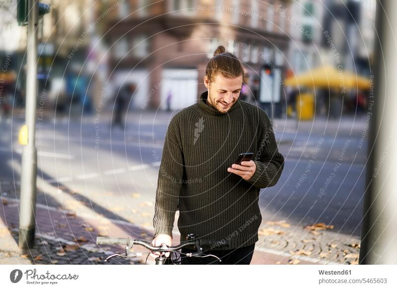 Smiling young man with bicycle in the city looking at cell phone eyeing men males view seeing viewing smiling smile Smartphone iPhone Smartphones bikes bicycles