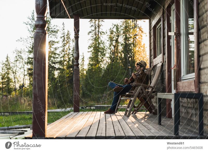 Young man sitting on veranda of a wood house, playing the ukulele Veranda Porch Patio Seated frame house wooden houses framehouses ukelele romantic lyrical