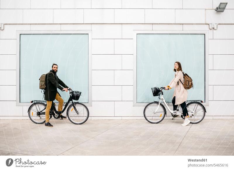 Portrait of man and woman with e-bikes standing at a building portrait portraits E-Bike Electric bicycle Electric Bike city town cities towns couple twosomes