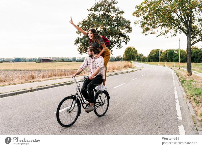 Happy young couple riding together on one bicycle on country road bikes bicycles rural road rural roads country roads twosomes partnership couples happiness