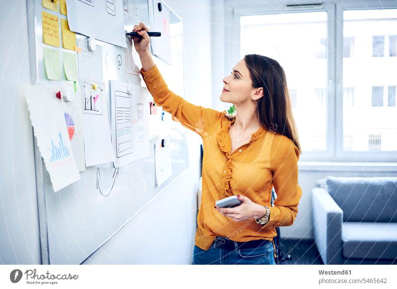 Smiling businesswoman taking notes on whiteboard in office offices office room office rooms white board smiling smile making a note note taking workplace