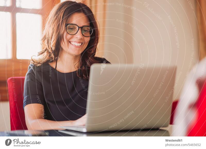 Happy businesswoman working at home while using laptop in living room color image colour image Spain indoors indoor shot indoor shots interior interior view