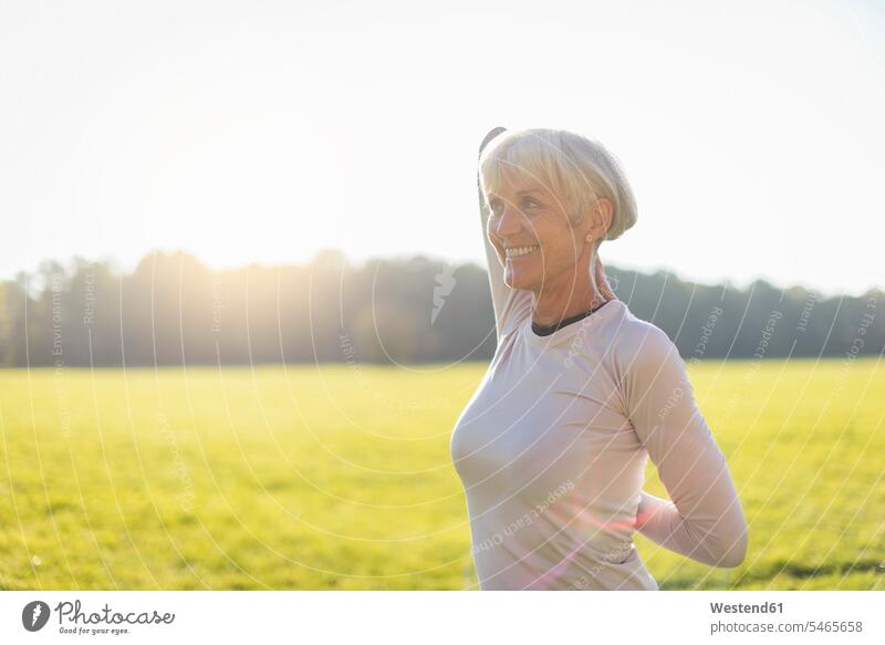 Smiling senior woman doing gymnastics on rural meadow senior women elder women elder woman old females country countryside stretching meadows Fitness training