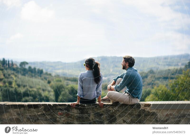 Couple looking at landscape while sitting on retaining wall against sky color image colour image Tuscany Italy tourism touristic leisure activity