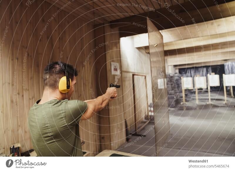 Man aiming with a pistol in an indoor shooting range gun guns pistols man men males weapon arms weapons Adults grown-ups grownups adult people persons
