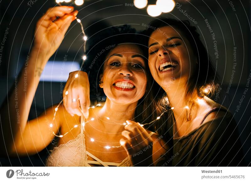 Close-up of cheerful female friends holding illuminated string lights at home color image colour image Portugal leisure activity leisure activities free time