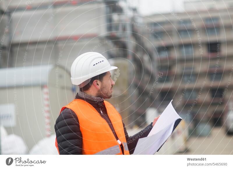 Man with plan wearing safety vest and hard hat at construction site hard hats hardhats hard-hat Building Site sites Building Sites construction sites plans man