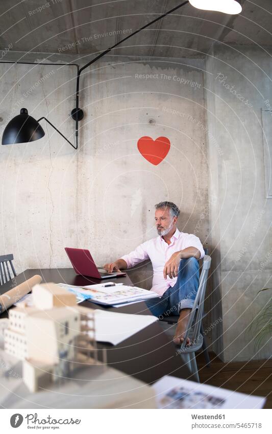 Businessman in a loft using laptop with documents and architectural model on table and heart on the wall lofts hearts heart shapes Architectural Model