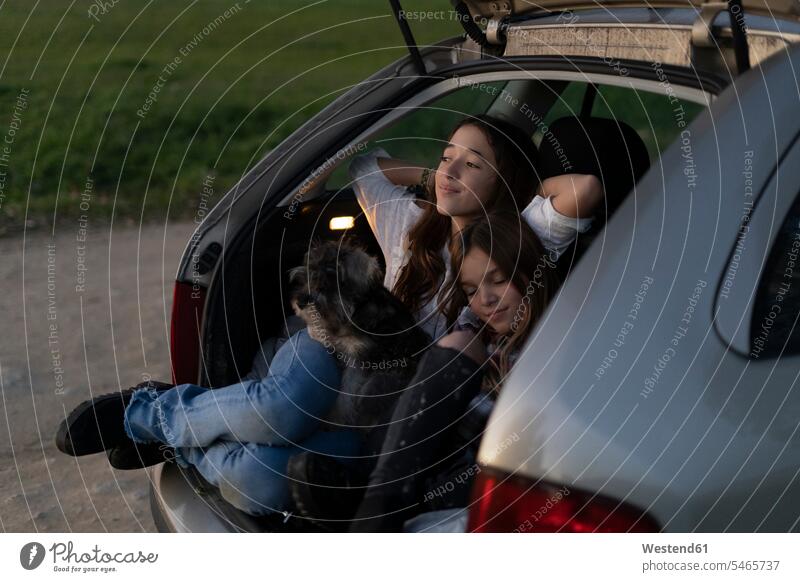 Two sisters in opened boot of parked car watching sunset sunsets sundown automobile Auto cars motorcars Automobiles sitting Seated looking looking at tail girl