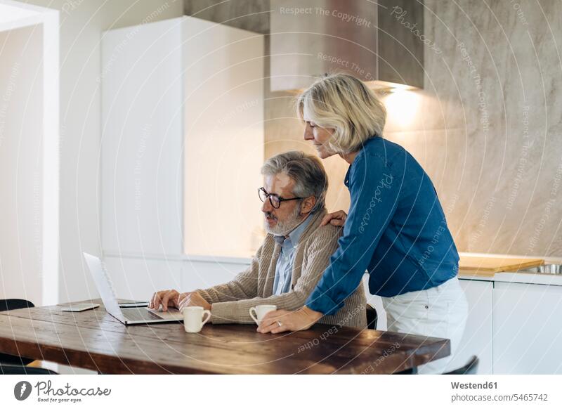 Mature man with wife using laptop on kitchen table at home human human being human beings humans person persons caucasian appearance caucasian ethnicity