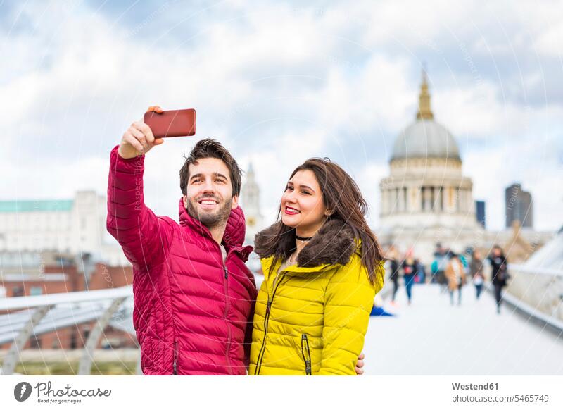 UK, London, portrait of smiling young couple taking selfie with cell phone in front of St Pauls Cathedral Smartphone iPhone Smartphones portraits twosomes