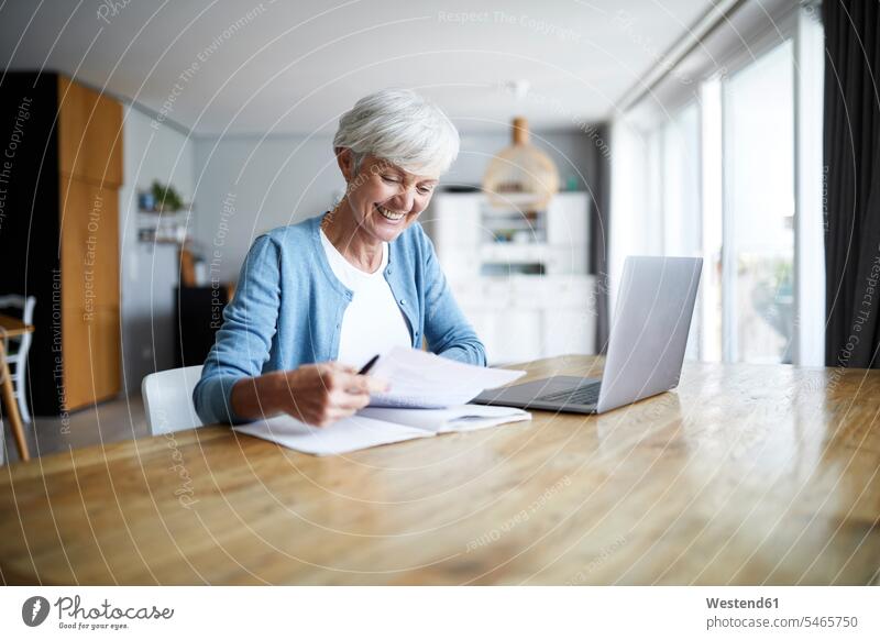 Smiling active senior woman doing paper work while sitting at home color image colour image indoors indoor shot indoor shots interior interior view Interiors