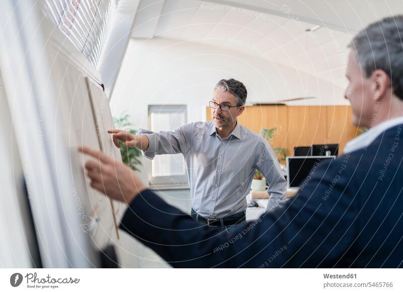 Mature male entrepreneur pointing while explaining strategy to businessman at office during meeting color image colour image Germany strategic Strategies
