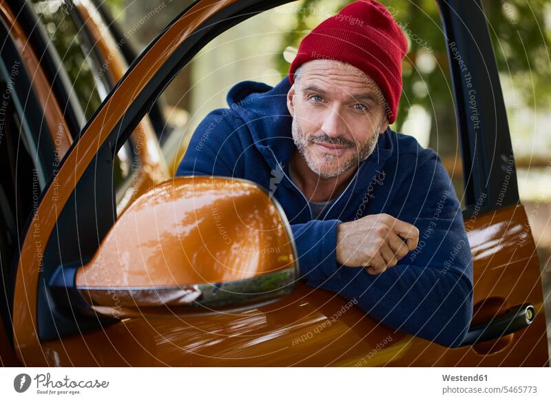 Portrait of bearded mature man wearing red cap leaning out of window of open car door portrait portraits car window car windows men males