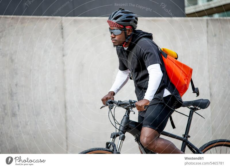 Stylish young man with messenger bag riding bicycle in the city human human being human beings humans person persons African black black ethnicity coloured 1