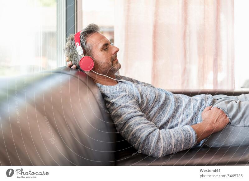 Relaxed mature man lying on couch at home wearing headphones laying down lie lying down relaxed relaxation headset settee sofa sofas couches settees men males