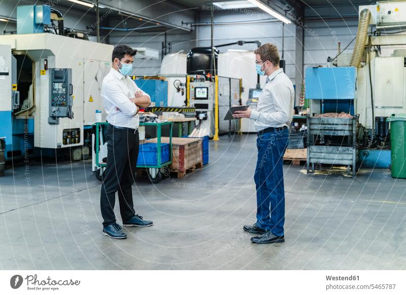 Male coworkers discussing while maintaining social distancing in factory color image colour image indoors indoor shot indoor shots interior interior view