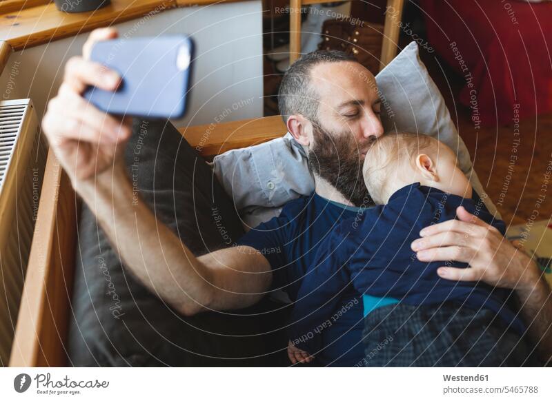 Man taking a selfie with his cute sleeping son on the sofa cushions couches settee settees sofas telecommunication phones telephone telephones cell phone