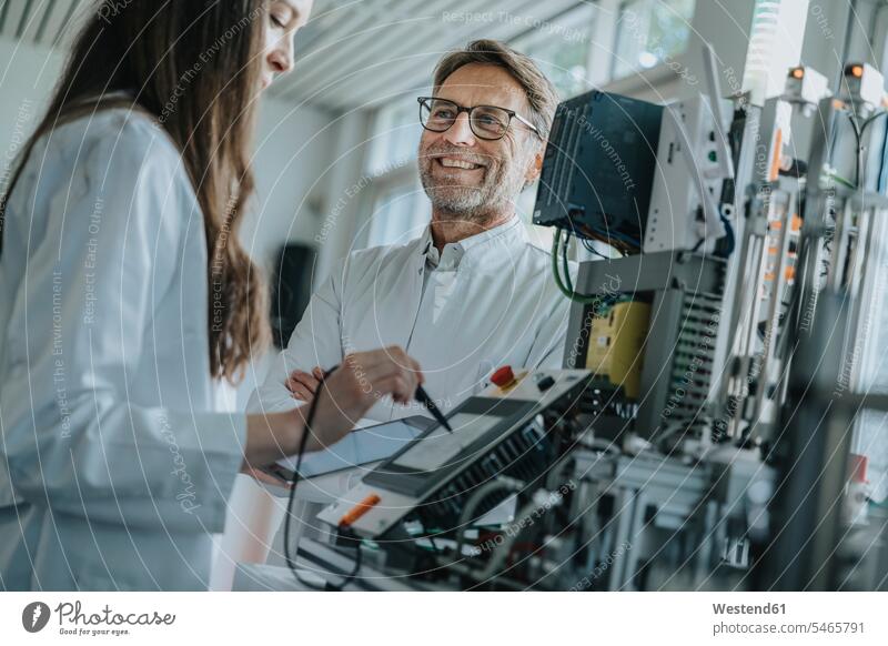 Smiling man looking at female colleague using machinery in laboratory color image colour image indoors indoor shot indoor shots interior interior view Interiors