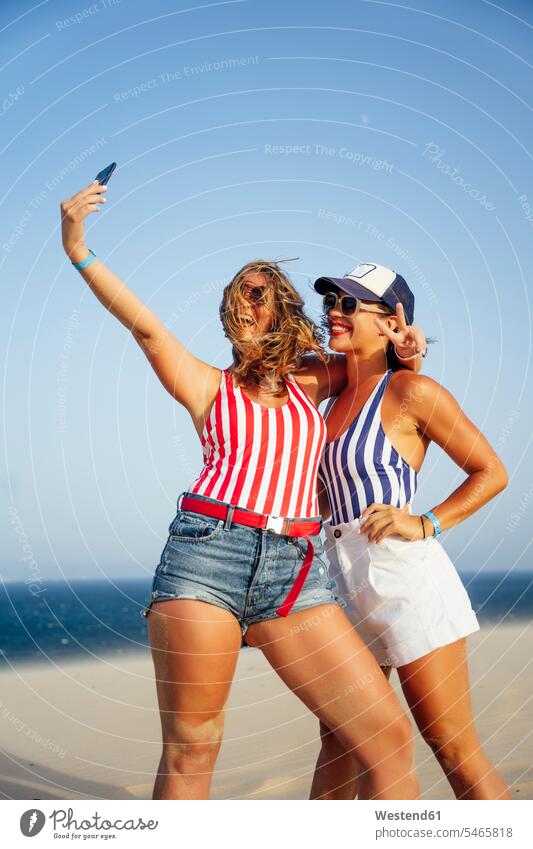 Cheerful female friends taking selfie while standing at beach against clear sky color image colour image Spain outdoors location shots outdoor shot