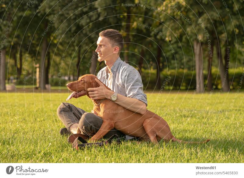 young man with his dog, cuddling on a meadow animals creature creatures pet Canine dogs smile Seated sit delight enjoyment Pleasant pleasure happy closeness