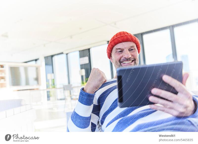 Happy man cheering while using digital tablet sitting at home color image colour image indoors indoor shot indoor shots interior interior view Interiors day