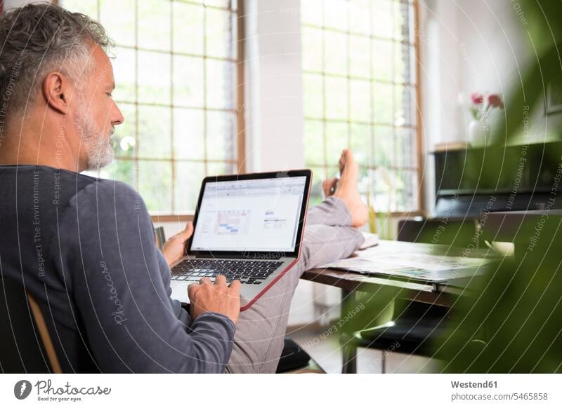 Mature man working from his home office with feet up, using laptop sitting Seated using a laptop Using Laptops Foot Up Legs Up loft lofts At Work