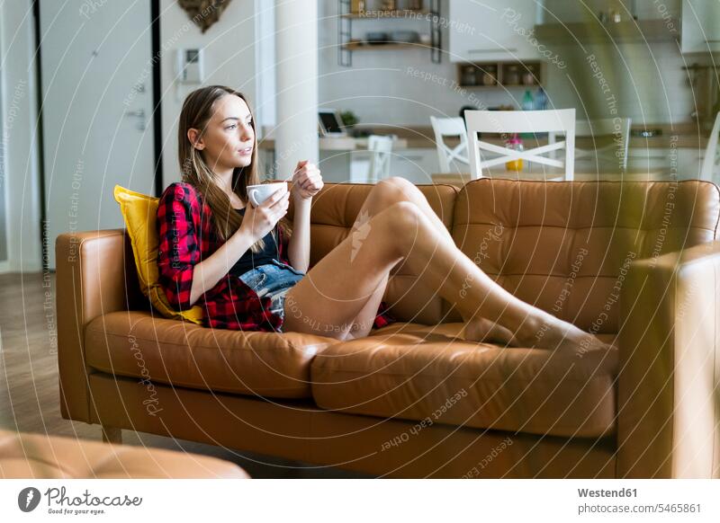 Relaxed young woman eating cereals in living room at home human human being human beings humans person persons celibate celibates singles solitary people