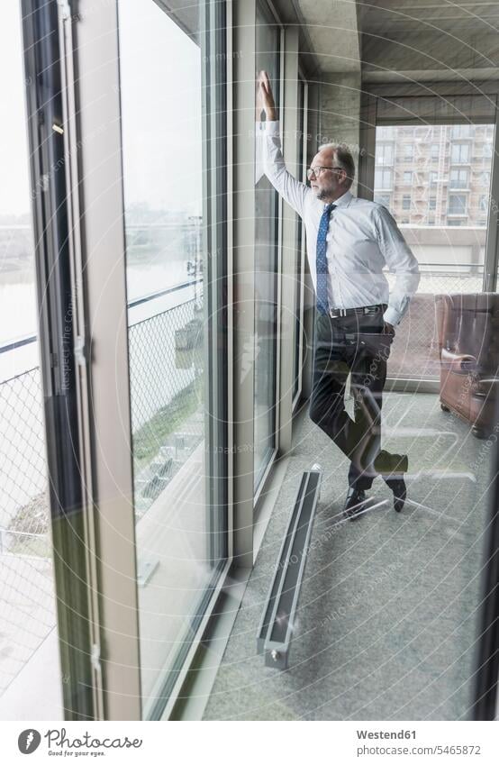 Serious mature businessman standing at the window looking out view seeing viewing Businessman Business man Businessmen Business men serious earnest Seriousness