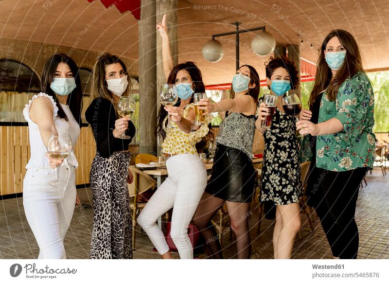 Young female customers holding drinks while standing at restaurant during pandemic color image colour image Spain indoors indoor shot indoor shots interior