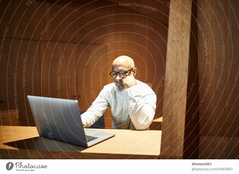 Portrait of mature man working on laptop at workspace with wood panelling At Work men males wall cladding Work Space workspaces Laptop Computers laptops