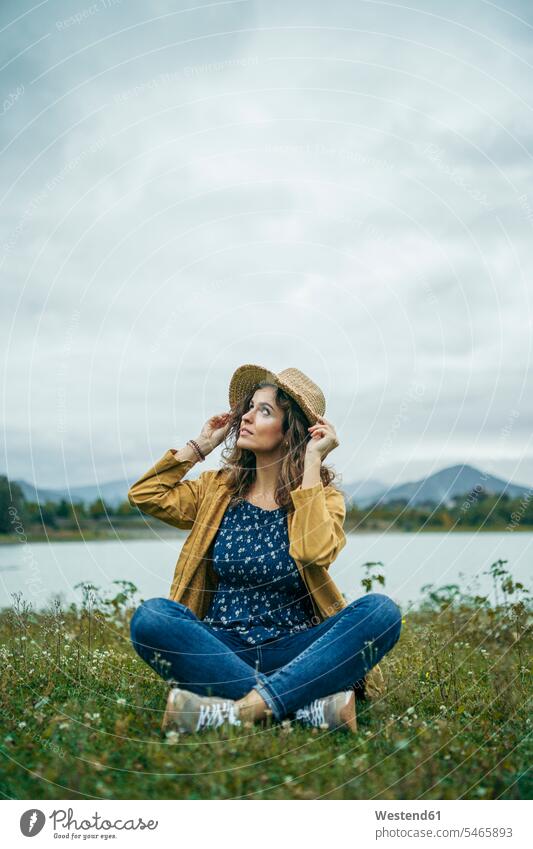Young woman wearing yellow coat sitting on a meadow and looking up human human being human beings humans person persons caucasian appearance caucasian ethnicity