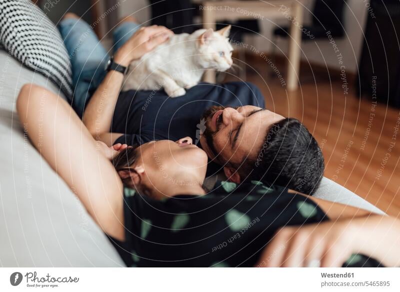 Young woman and mid adult man lying down on sofa shares tenderness with cat at home color image colour image indoors indoor shot indoor shots interior