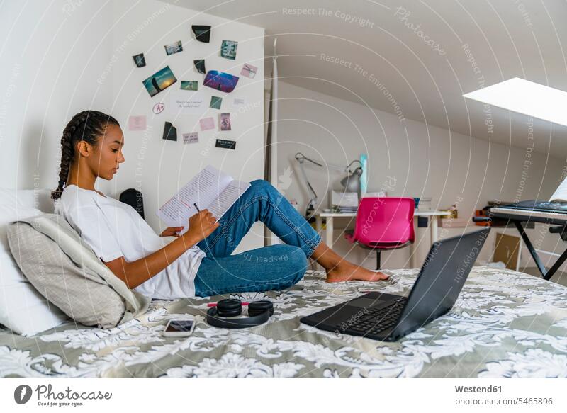 Teenage girl writing in exercise book while sitting on bed at home color image colour image indoors indoor shot indoor shots interior interior view Interiors