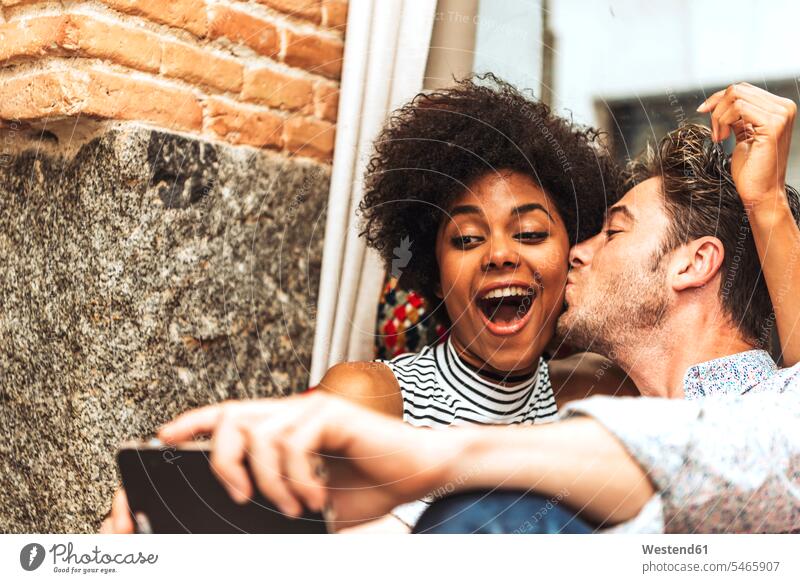 Close-up of man kissing cheerful girlfriend while taking selfie with her in coffee shop color image colour image indoors indoor shot indoor shots interior