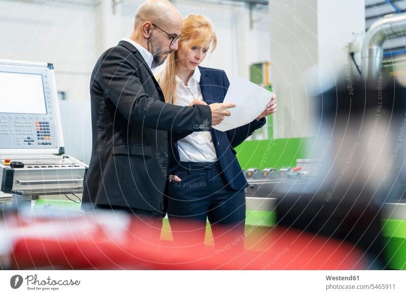 Businessman and businesswoman looking at plan in factory eyeing factories Business man Businessmen Business men businesswomen business woman business women