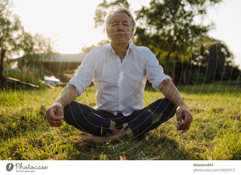 Man practicing yoga while sitting in lotus position at yard color image colour image full length full-length full body full-body full shot outdoors