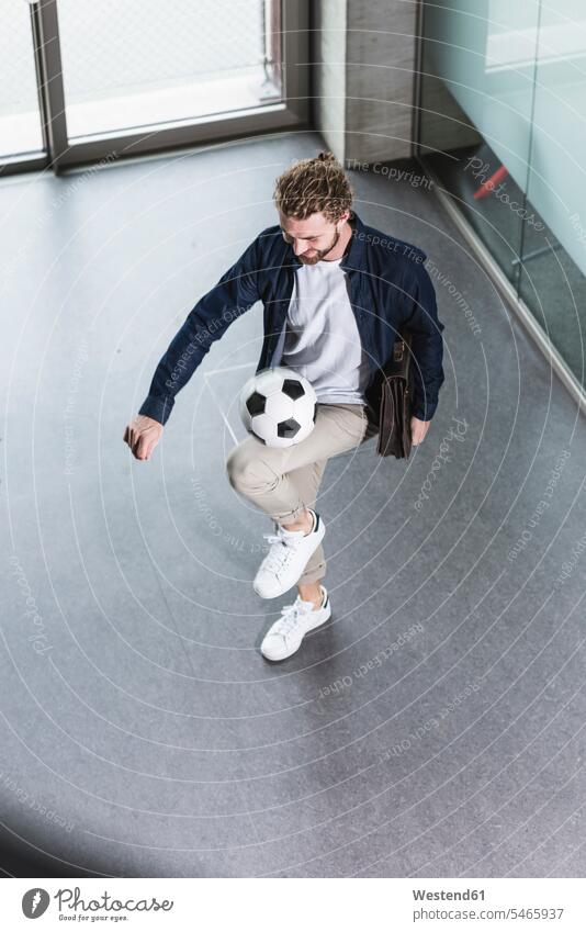 Casual young businessman playing football in office Businessman Business man Businessmen Business men offices office room office rooms soccer ball soccer balls